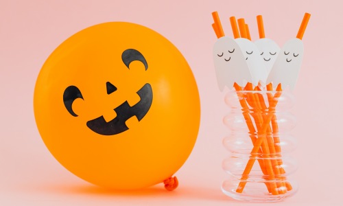 Orange ballon decorated with a spooky halloween face next to a glass full of straws with a ghost on them